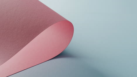 Nahaufnahme-Eines-Rosafarbenen,-Aufgerollten-Stück-Papier-Auf-Hellblauem-Hintergrund-Mit-Kopierraum-In-Zeitlupe