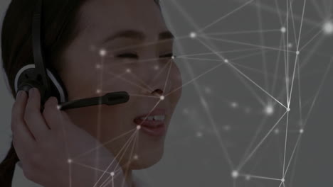 Animation-of-network-of-connections-over-asian-businesswoman-using-phone-headset-in-office