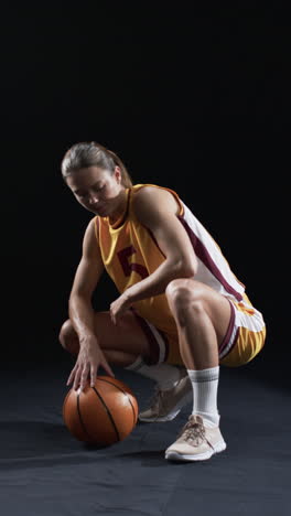 Vertical-video:-Caucasian-female-athlete-with-basketball-in-sportswear,-black-background