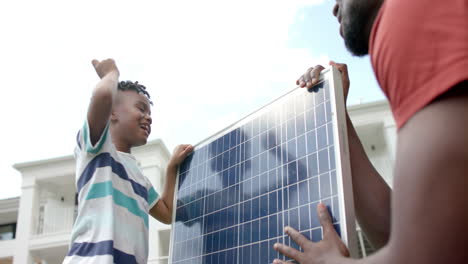 African-American-father-and-son-handle-a-solar-panel-outdoors-at-home