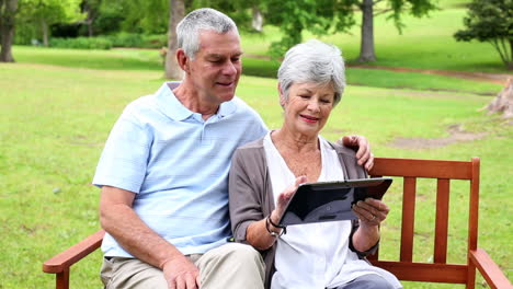 Retired-couple-sitting-on-a-park-bench-using-a-tablet