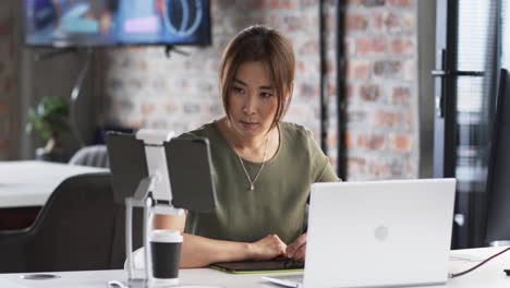 Asian-senior-professional-looking-at-laptop,-wearing-green-top