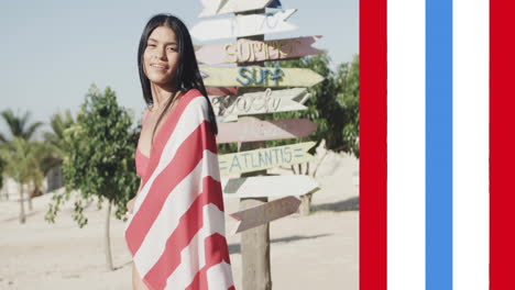 Animation-of-usa-flag-stripes-over-happy-biracial-woman-in-american-flag-dancing-on-sunny-beach