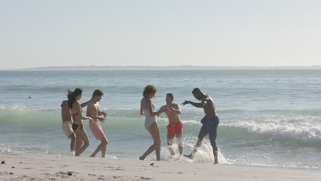 Un-Grupo-Diverso-De-Jóvenes-Disfruta-De-Un-Día-En-La-Playa,-Corriendo-Por-La-Orilla