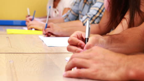 Students-sitting-in-a-line-taking-notes-in-classroom