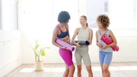 Three-women-are-standing-in-bright-yoga-studio,-holding-mats