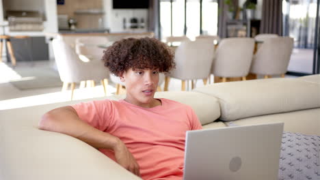 A-young-biracial-man-is-working-on-a-laptop-on-the-couch-at-home