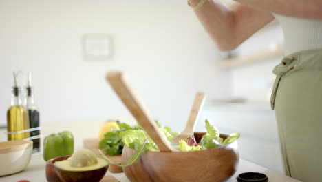 A-mature-Caucasian-woman-preparing-salad-in-bright-kitchen