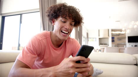 A-young-biracial-man-is-engaged-with-his-smartphone-on-a-couch-at-home