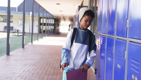 In-a-school-hallway,-a-young-African-American-student-stands-by-blue-lockers-with-copy-space