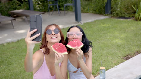 Two-biracial-female-friends-enjoying-watermelon-and-taking-selfies-at-home