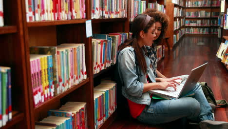 Smiling-students-studying-together-sitting-on-floor-in-library