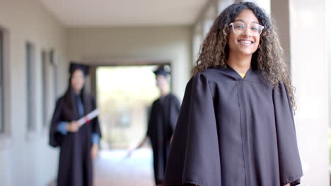Biracial-teenage-girl-in-graduation-gown-smiles-proudly,-with-copy-space