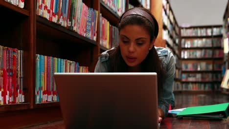 Student-lying-on-floor-in-library-using-laptop