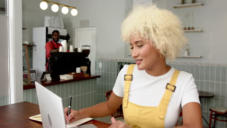 Una-Joven-Birracial-Con-Cabello-Rubio-Rizado-Trabaja-En-Su-Computadora-Portátil-En-Un-Café