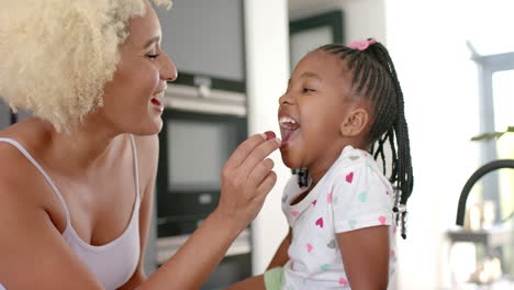 Biracial-mom-and-daughter-share-joyful-moment-with-strawberry-at-home.