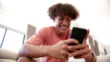 A-young-biracial-man-is-engaged-with-his-smartphone,-on-the-couch-at-home