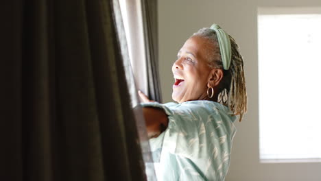 African-American-senior-woman-opening-curtains,-looking-outside