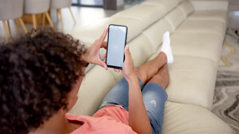 A-young-biracial-man-is-interacting-with-a-smartphone-on-a-couch-at-home