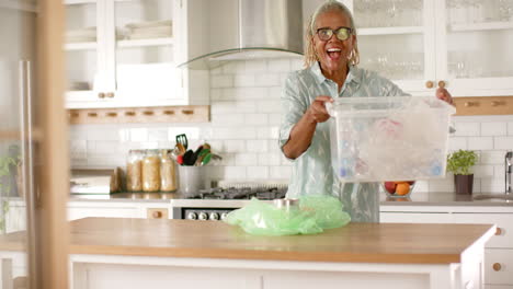 African-American-senior-woman-holding-recycling-bin-in-kitchen