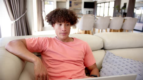 A-young-biracial-man-with-curly-hair-sits-thoughtfully-on-a-sofa