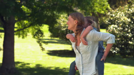 Young-mother-giving-her-daughter-a-piggy-back-in-the-park