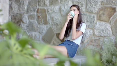 Teenage-Caucasian-girl-with-long-brown-hair-enjoys-a-drink-on-a-stone-ledge-at-home-with-copy-space
