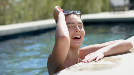 A-teenage-Caucasian-girl-is-laughing-by-a-poolside,-her-wet-hair-slicked-back