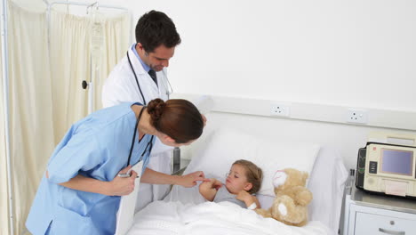 Sick-little-girl-lying-in-bed-talking-to-nurse-and-doctor