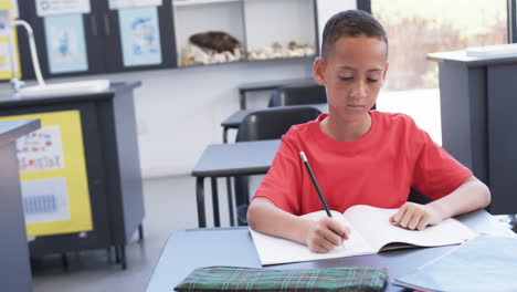 A-young-African-American-student-writes-intently-in-classroom,-copy-space