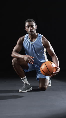 Vertikales-Video:-Afroamerikanischer-Männlicher-Athlet-Posiert-Mit-Basketball,-Schwarzer-Hintergrund