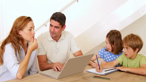 Parents-using-laptop-and-children-colouring-at-the-table