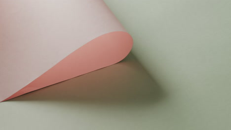 Close-up-of-pink-rolled-paper-on-pale-green-background-with-copy-space-in-slow-motion