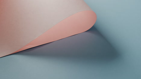 Close-up-of-pink-rolled-paper-on-blue-background-with-shadow-and-copy-space,-in-slow-motion