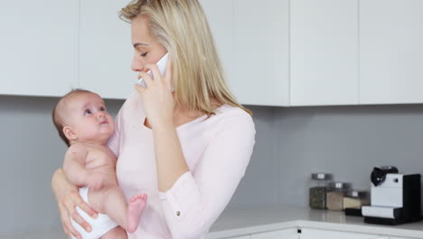 Madre-Haciendo-Una-Llamada-Telefónica-Y-Sosteniendo-A-Un-Bebé