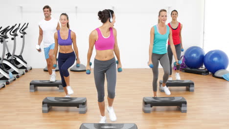 Aerobics-class-stepping-together-led-by-instructor-and-lifting-dumbbells