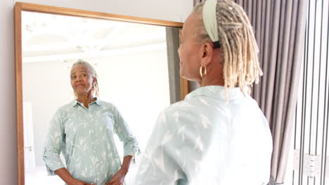 African-American-senior-woman-looking-at-mirror,-wearing-light-blue-shirt