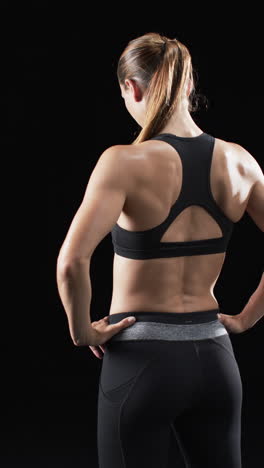 Vertikales-Video:-Kaukasische-Sportlerin-Zeigt-Starke-Rückenmuskulatur,-Schwarzer-Hintergrund
