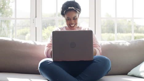 Una-Mujer-Afroamericana-Sonríe-Usando-Una-Computadora-Portátil-En-Un-Sofá-En-Casa