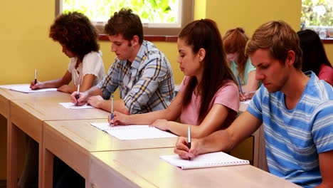 Konzentrierte-Schüler-Sitzen-In-Einer-Reihe-Und-Schreiben-Im-Klassenzimmer