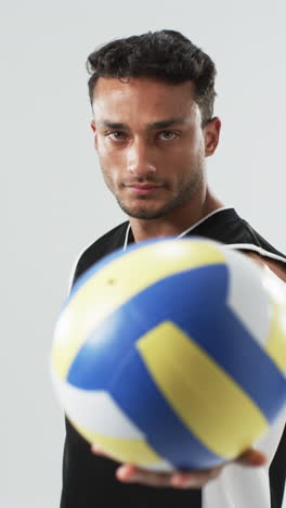 Vertical-video:-Biracial-male-athlete-holding-volleyball,-white-background