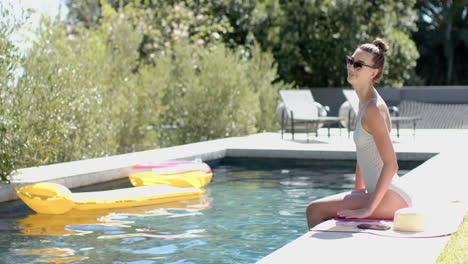 A-teenage-Caucasian-girl-with-brown-hair-tied-back-is-sitting-poolside-with-copy-space