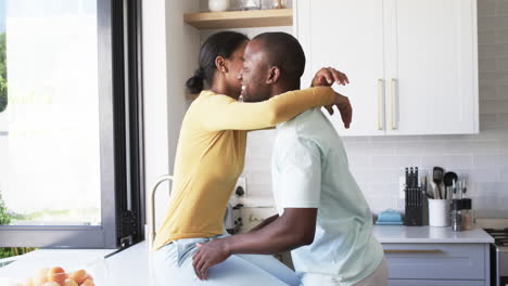 A-young-African-American-couple-shares-a-warm-embrace,-hugging-in-a-bright-kitchen