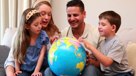Happy-young-family-sitting-on-sofa-looking-at-globe