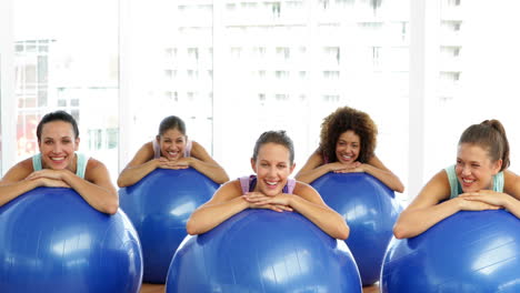 Fitness-class-in-studio-leaning-on-exercise-balls-smiling-at-camera