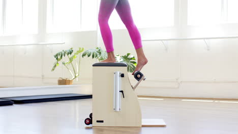 Caucasian-woman-wearing-pink-leggings-is-exercising-on-Pilates-machine