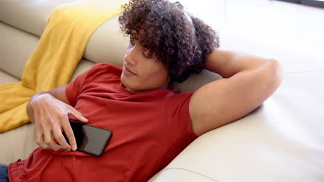 A-young-biracial-man-relaxes-with-headphones-on-sofa-at-home