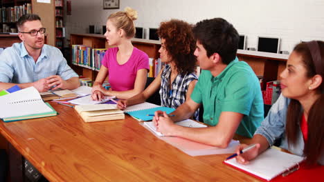 Jóvenes-Estudiantes-Estudiando-Juntos-En-La-Biblioteca-Con-Su-Maestro
