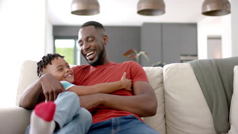 African-American-man-shares-a-joyful-moment-with-his-son-on-a-sofa-at-home-with-copy-space
