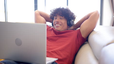 A-young-biracial-man-relaxes-on-a-sofa-at-home,-using-a-laptop